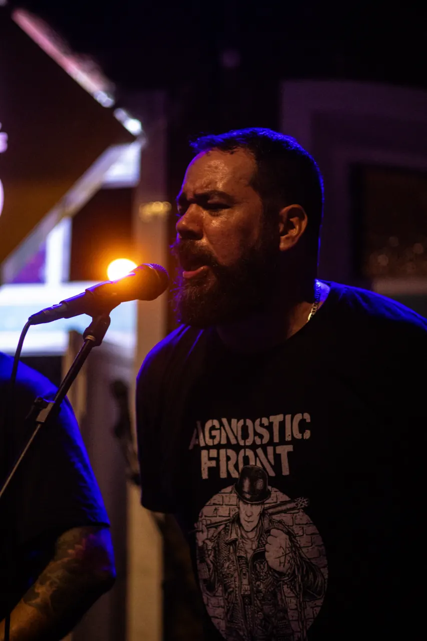 Vocalista barbudo canta de olhos fechados sob luz azul.