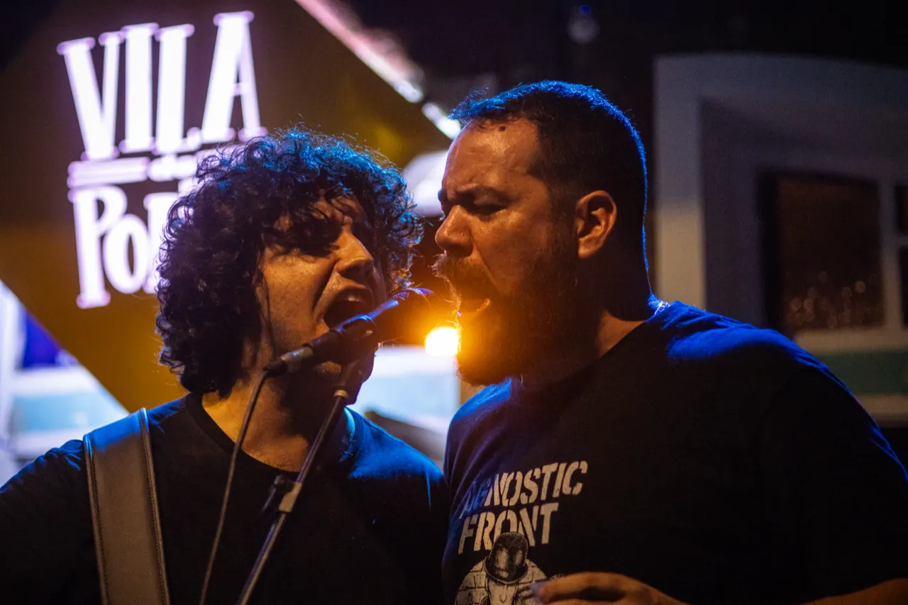 Dois vocalistas dividem o microfone diante da placa do Vila do Porto.