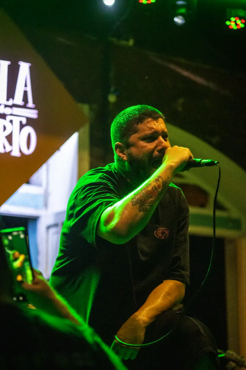 Vocalista sob luz verde, com o braço tatuado e o microfone na mão.