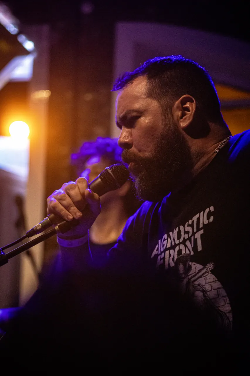 Vocalista canta de perfil sob luz azul e roxa.